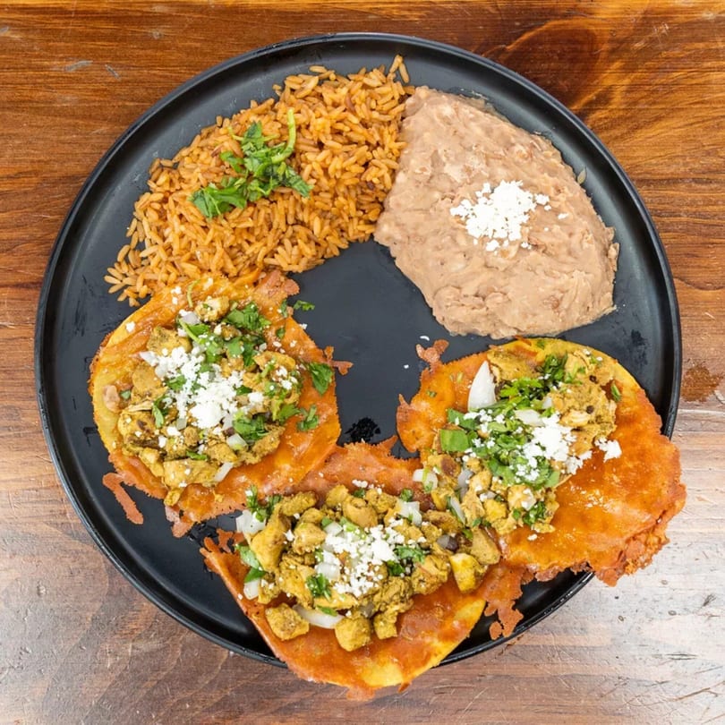 Three chicken enchiladas with rice and refried beans on a black plate.