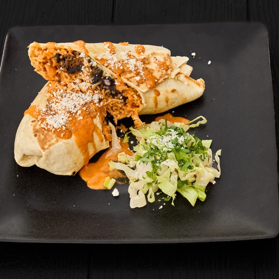 A grilled burrito filled with rice and black beans, topped with orange sauce and cheese, served with a fresh green salad.