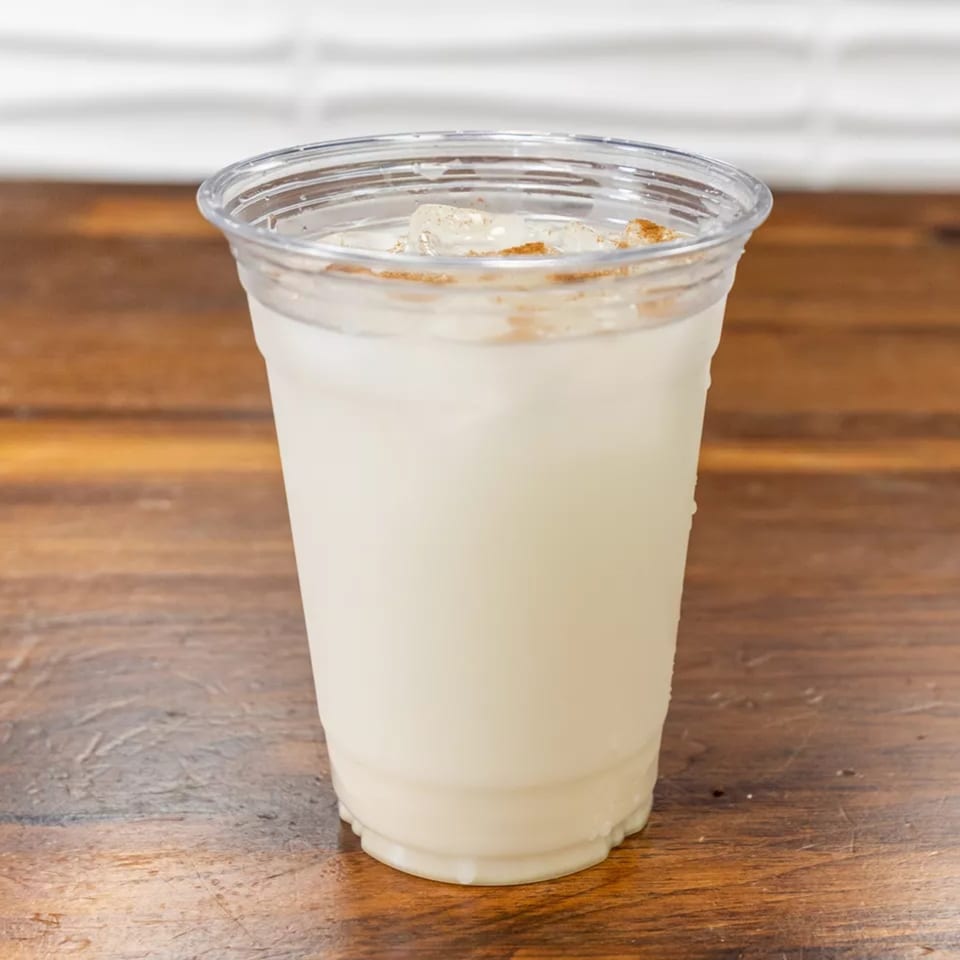 Horchata drink in a clear plastic cup with ice and cinnamon on a wooden table.