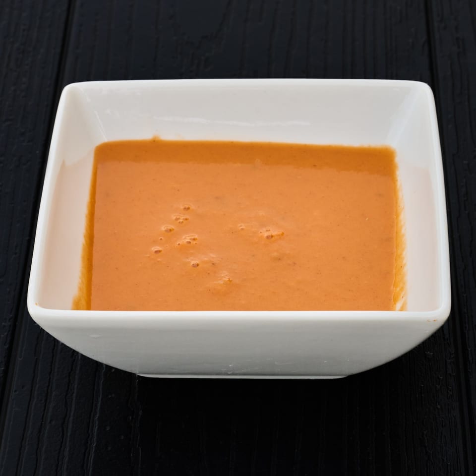 Square white bowl filled with smooth orange dipping sauce on a black wooden table.