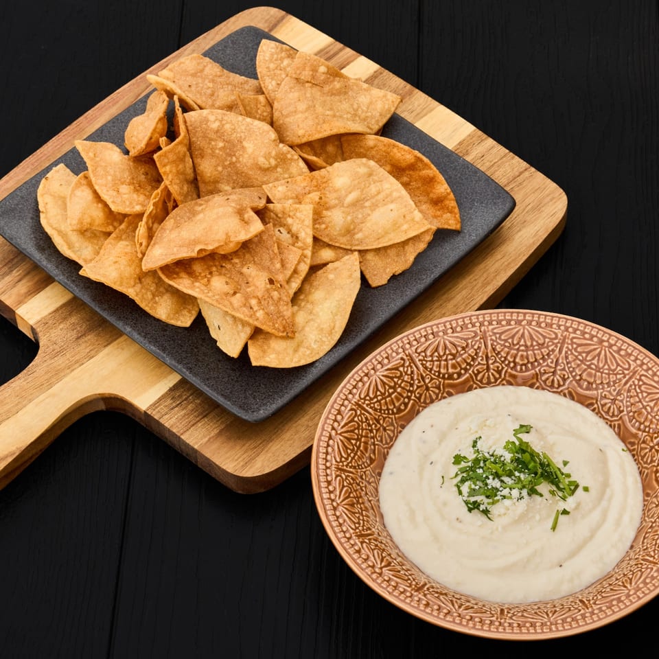 Crispy tortilla chips on a black plate beside creamy dip garnished with cilantro and cheese.