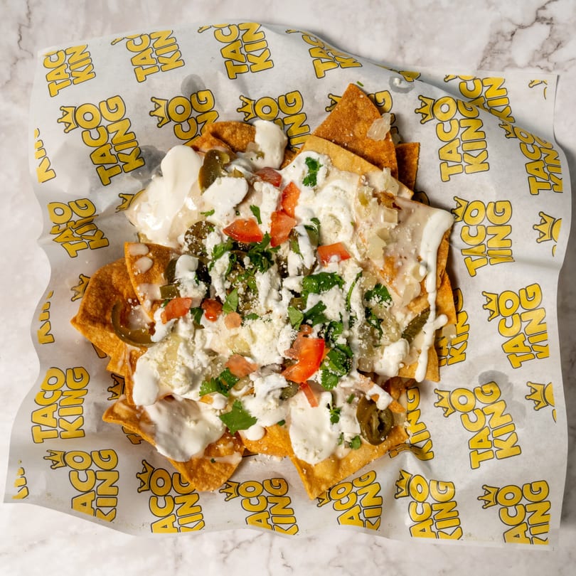 Taco King nachos with cheese, jalapeños, tomatoes, onions, and cilantro on branded paper.