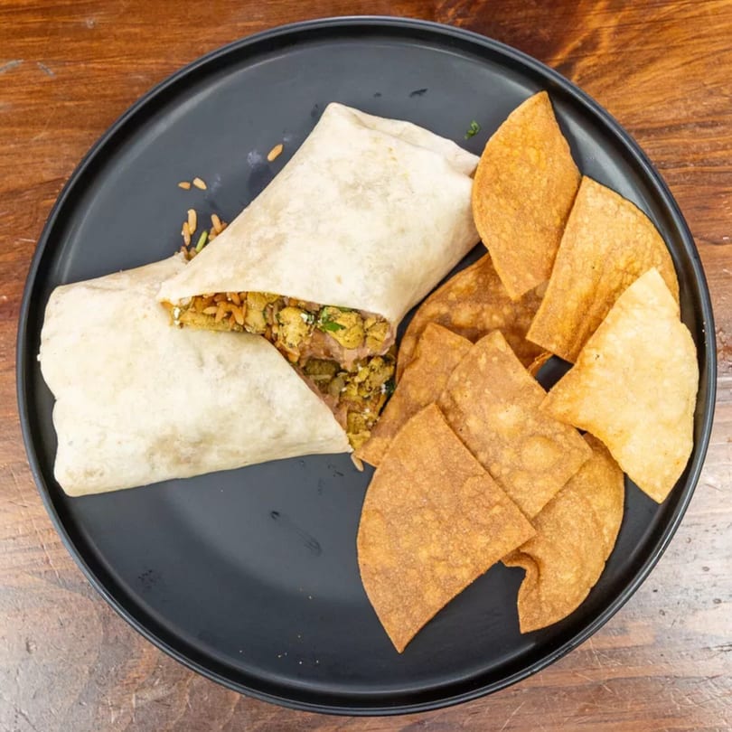 A black plate holds a burrito, cut open to show its filling, and a pile of tortilla chips.