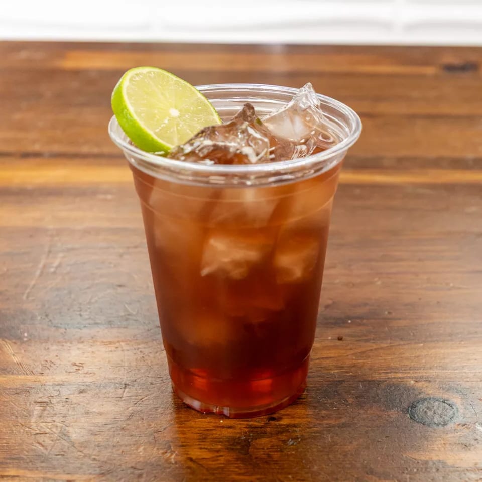 Iced tea with a lime wedge and ice in a clear plastic cup on a wooden table.