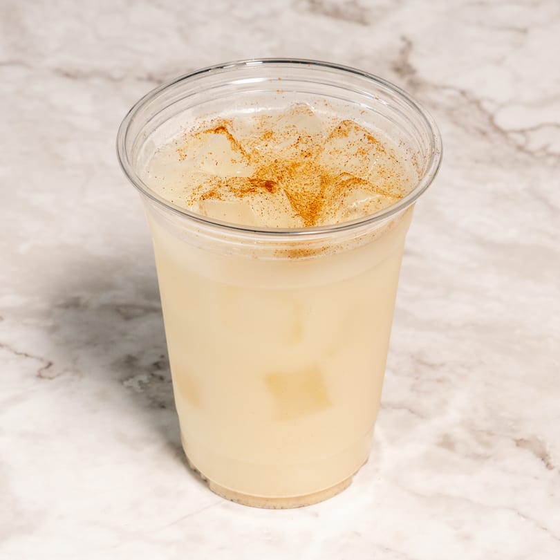 Horchata drink in a clear plastic cup with ice and a sprinkle of cinnamon on a marble surface.