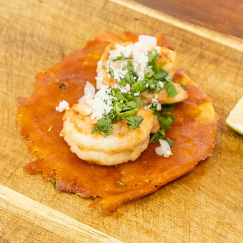 Shrimp taco on a red tortilla, topped with crumbled white cheese and fresh cilantro, on a wooden board.