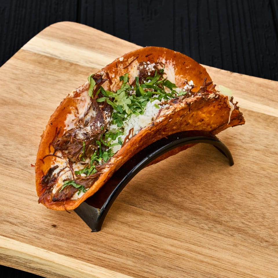 Birria tacos with shredded beef, white cheese, and cilantro served in a black taco holder on a wooden board.