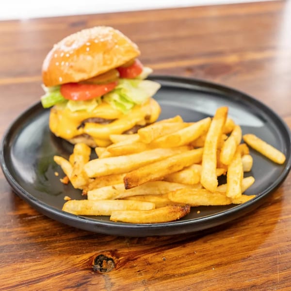 Cheeseburger with lettuce, tomato, and pickles, served with a side of golden french fries on a black plate.