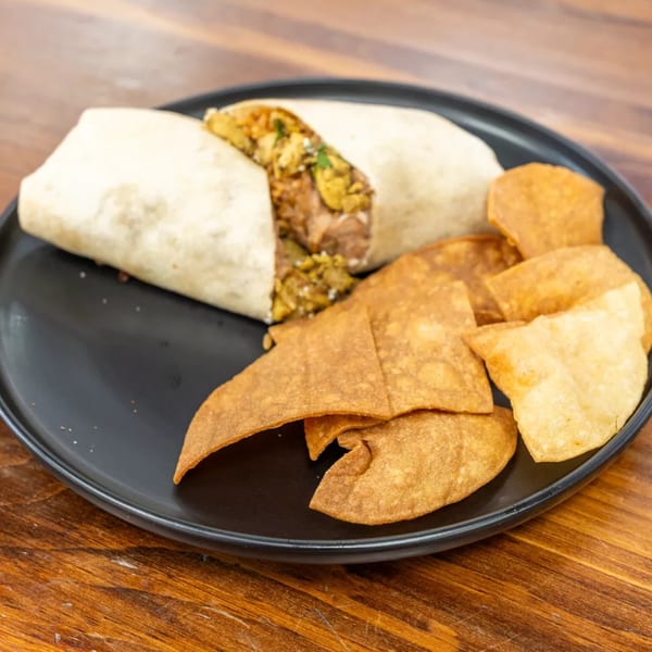 A breakfast burrito, cut open to show its filling, served with a side of tortilla chips on a black plate.