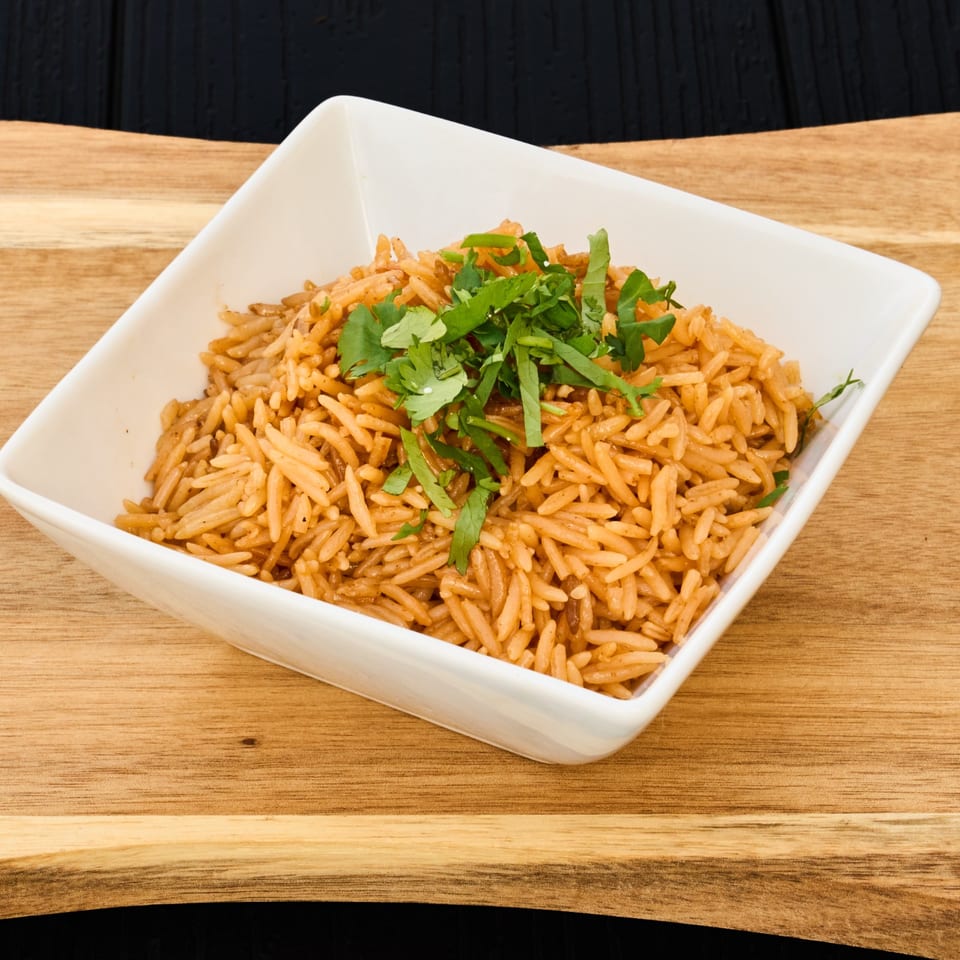 Seasoned orange rice topped with fresh cilantro in a white square bowl on a wooden table.