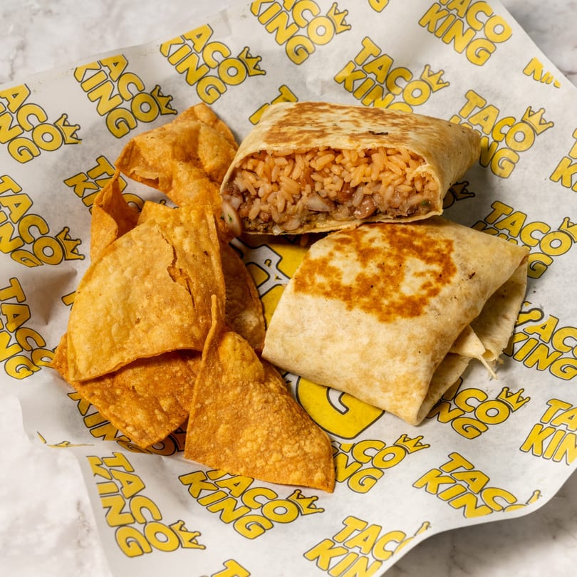 Two burritos and a pile of tortilla chips on Taco King branded paper.